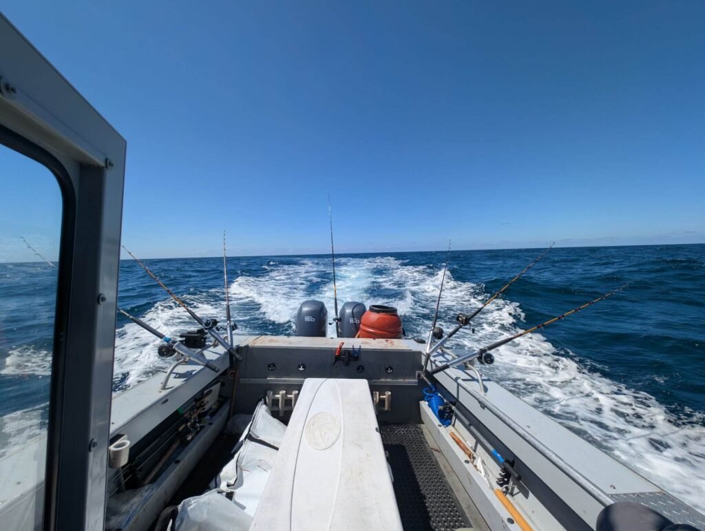 Fishing charter boat cruising offshore with multiple trolling rods set and ocean wake behind.