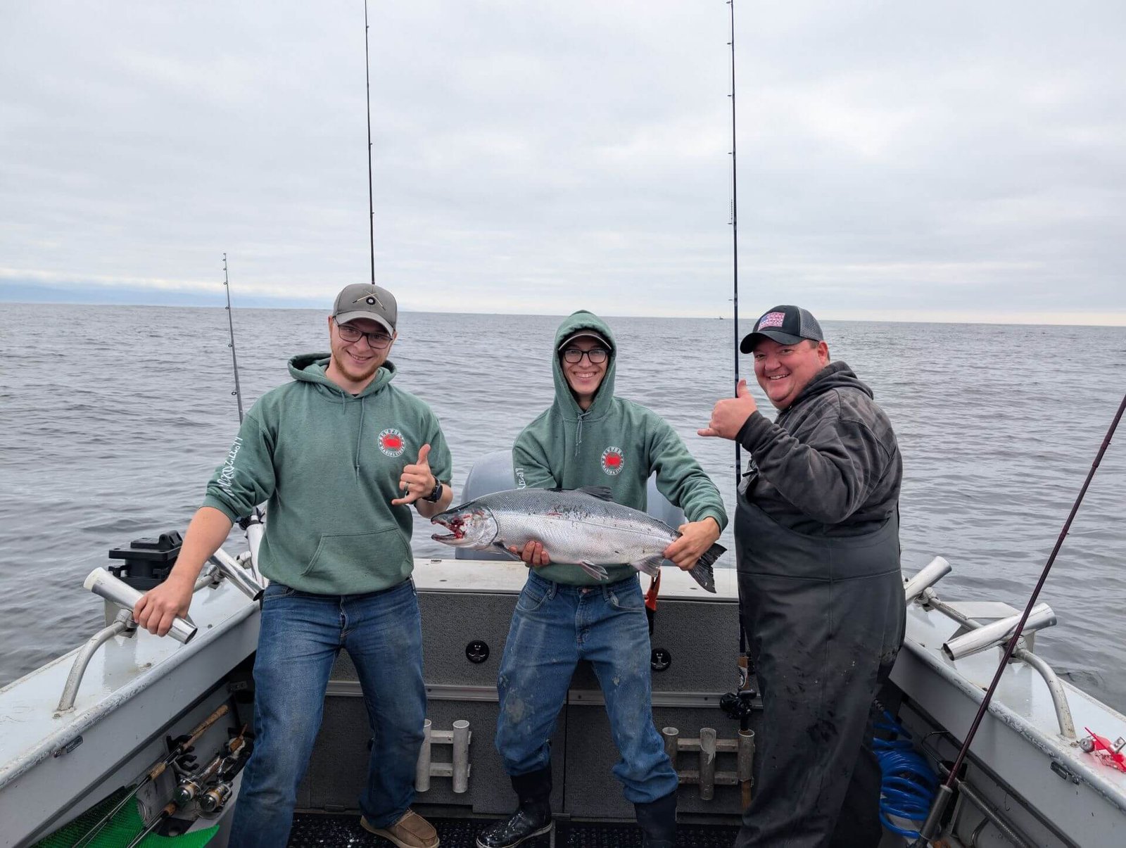 Three anglers on a fishing charter boat holding a large salmon caught offshore near Newport Oregon.