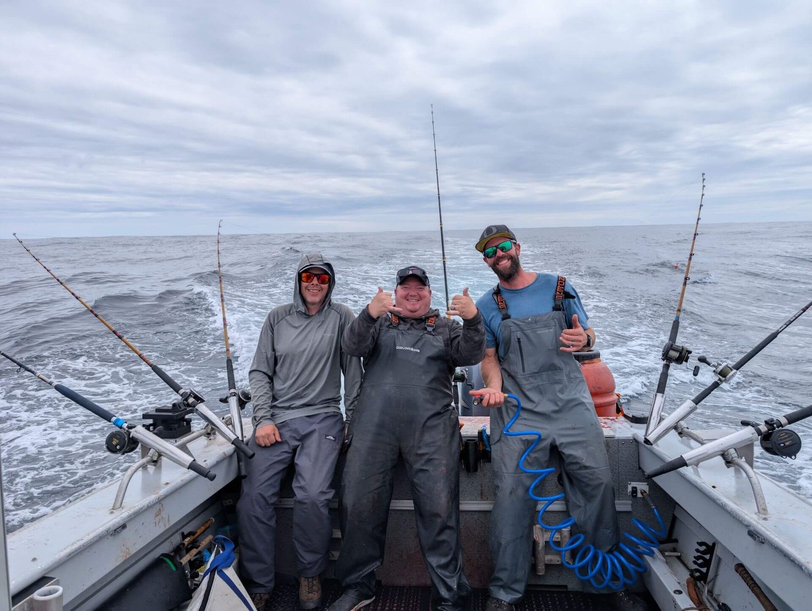 Three anglers smiling on the back deck of a fishing charter boat during an offshore trip.